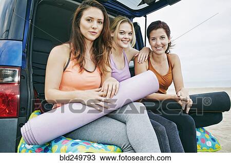 Stock Image - Portrait of smiling Caucasian women sitting in hatch of car on beach. Fotosearch