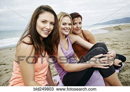 Stock Image - Portrait of smiling Caucasian women sitting on beach. Fotosearch