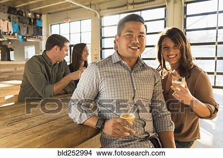 Picture - Portrait of smiling couple drinking beer with friends in brew pub. Fotosearch