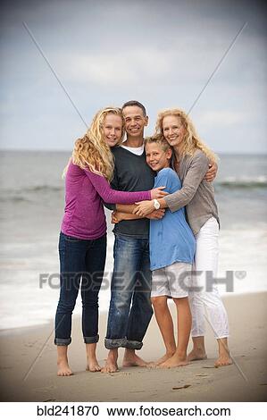 Stock Image - Portrait of smiling family hugging on beach. Fotosearch