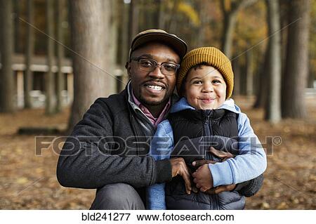 Stock Photo - Portrait of smiling father and son hugging in park. Fotosearch