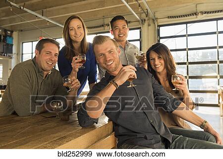 Stock Photo - Portrait of smiling friends drinking beer in brew pub. Fotosearch