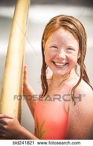 Stock Image - Portrait of smiling girl holding surfboard. Fotosearch