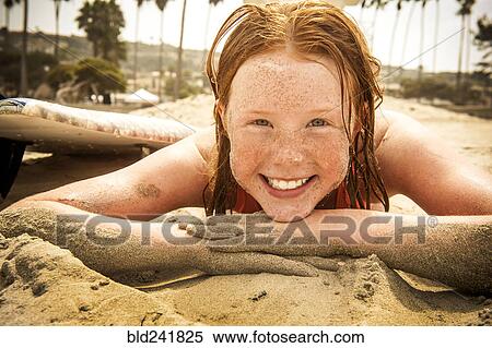 Stock Photography - Portrait of smiling girl laying on beach covered with sand. Fotosearch