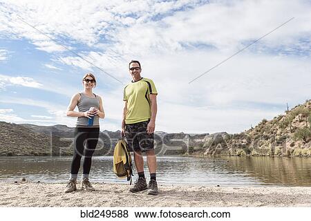 Stock Photo - Portrait of smiling hikers standing at lake. Fotosearch
