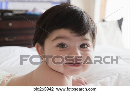 Stock Image - Portrait of smiling Hispanic baby boy laying on bed. Fotosearch
