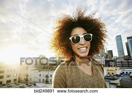 Stock Image - Portrait of smiling Hispanic woman on urban rooftop at sunset. Fotosearch