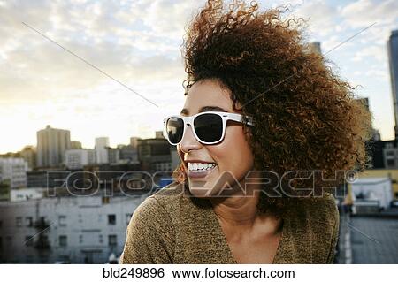 Stock Photograph - Portrait of smiling Hispanic woman on urban rooftop at sunset. Fotosearch