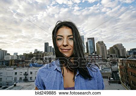 Stock Photography - Portrait of smiling Hispanic woman on urban rooftop. Fotosearch