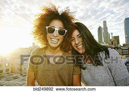 Stock Image - Portrait of smiling Hispanic women on urban rooftop at sunset. Fotosearch