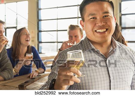 Stock Image - Portrait of smiling man drinking beer with friends in brew pub. Fotosearch