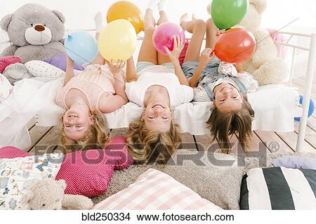 Picture - Portrait of smiling Middle Eastern sisters laying on bed. Fotosearch