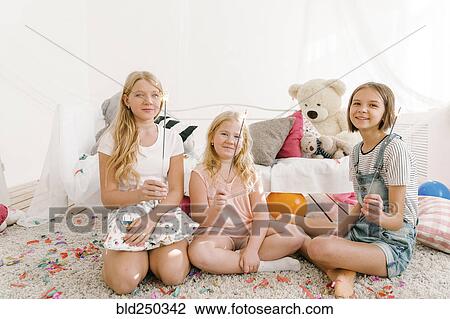 Stock Image - Portrait of smiling Middle Eastern sisters holding sparklers in bedroom. Fotosearch