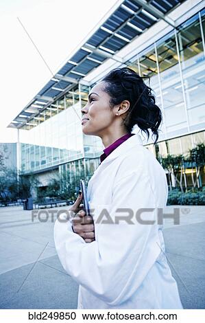 Stock Image - Portrait of smiling Mixed Race doctor holding digital tablet outdoors. Fotosearch