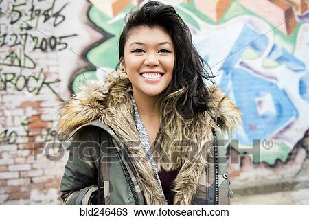 Stock Image - Portrait of smiling Mixed Race woman standing near graffiti. Fotosearch