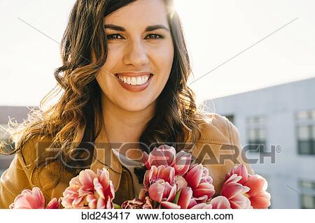 Stock Photo - Portrait of smiling Mixed Race woman holding flowers. Fotosearch