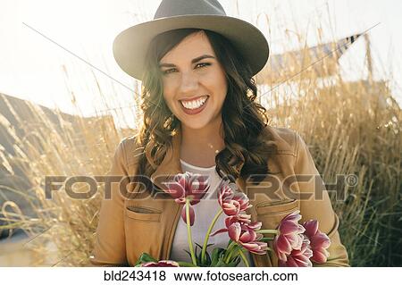 Stock Photo - Portrait of smiling Mixed Race woman wearing hat holding flowers. Fotosearch