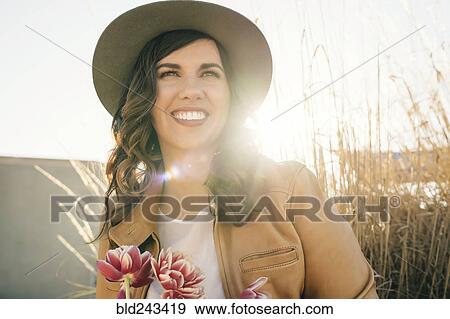 Stock Photo - Portrait of smiling Mixed Race woman wearing hat holding flowers. Fotosearch