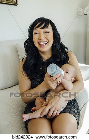 Picture - Portrait of smiling mother feeding bottle to baby daughter. Fotosearch