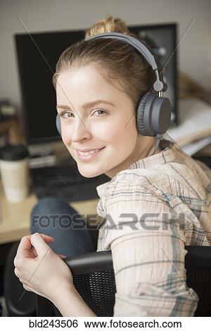 Stock Photograph - Portrait of smiling woman using computer and listening to headphones. Fotosearch