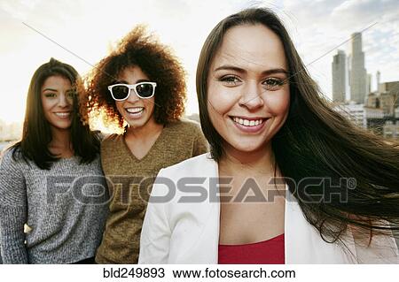 Stock Image - Portrait of smiling women on urban rooftop at sunset. Fotosearch