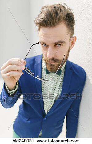 Stock Image - Portrait of stylish Middle Eastern man with beard holding eyeglasses. Fotosearch