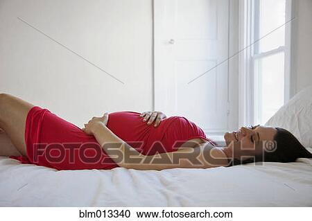 Stock Image - Pregnant Caucasian woman laying on bed. Fotosearch
