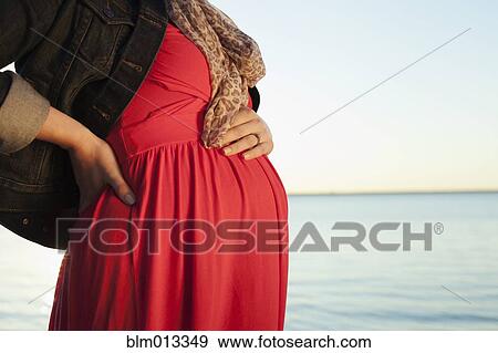Stock Photo - Pregnant Caucasian woman standing near ocean. Fotosearch