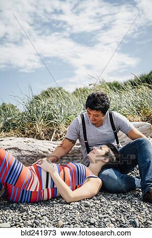Stock Image - Pregnant lesbian couple relaxing on rocky beach. Fotosearch