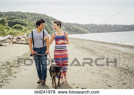 Stock Photo - Pregnant lesbian couple walking dog on beach. Fotosearch