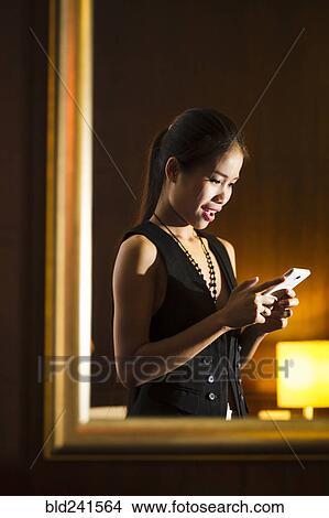 Reflection in mirror of Asian woman texting on cell phone View Large Photo Image Picture - Reflection in mirror of Asian woman texting on cell phone. Fotosearch