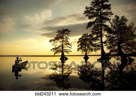 Stock Image - Reflection of Caucasian boy in canoe near trees in river. Fotosearch