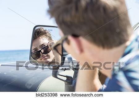 Stock Photo - Reflection of Caucasian man in side-view mirror of car on beach. Fotosearch