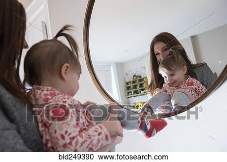 Stock Image - Reflection of Caucasian mother and baby daughter in mirror. Fotosearch