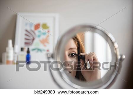 Stock Image - Reflection of Caucasian woman applying mascara in mirror. Fotosearch