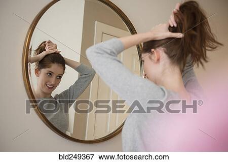 Stock Photo - Reflection of Caucasian woman in mirror pulling back hair. Fotosearch