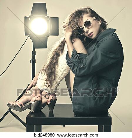 Stock Image - Retro Caucasian girl sitting on table near spotlight. Fotosearch