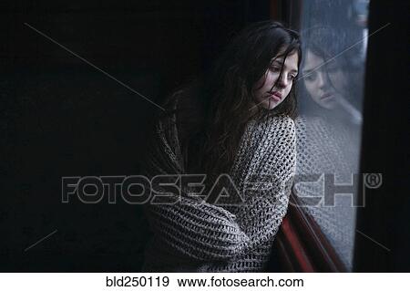Sad Caucasian woman wrapped in scarf leaning on window View Large Photo Image Stock Photo - Sad Caucasian woman wrapped in scarf leaning on window. Fotosearch