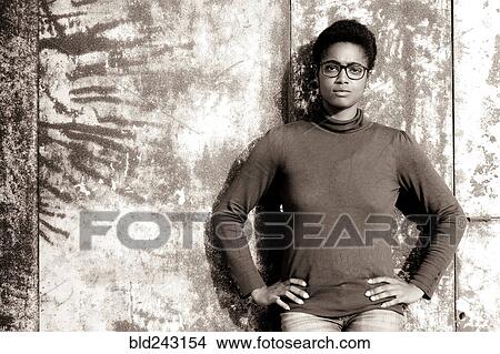Picture - Serious African American woman leaning on rusty metal wall. Fotosearch