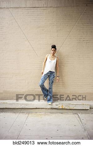 Stock Image - Serious African American woman standing on ledge at brick wall. Fotosearch