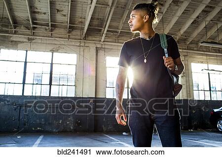 Stock Image - Serious androgynous Mixed Race woman carrying backpack. Fotosearch