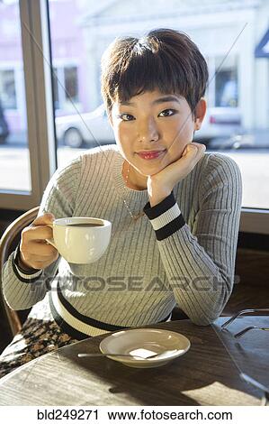 Stock Image - Serious Asian teenage girl drinking coffee in coffee shop. Fotosearch