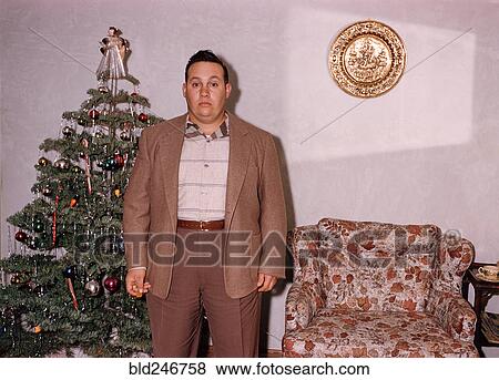 Stock Photo - Serious Caucasian man posing near Christmas tree. Fotosearch