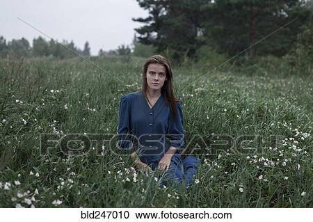 Stock Image - Serious Caucasian teenage girl sitting in field of wildflowers. Fotosearch