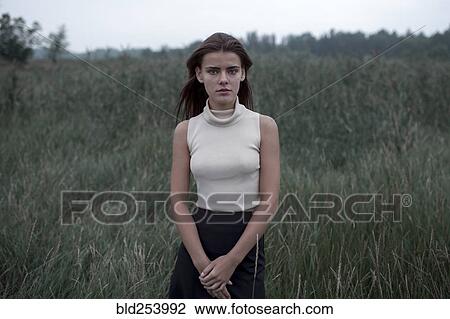 Stock Image - Serious Caucasian teenage girl standing in field. Fotosearch