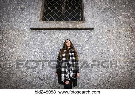 Stock Photo - Serious Caucasian woman leaning on wall under window. Fotosearch