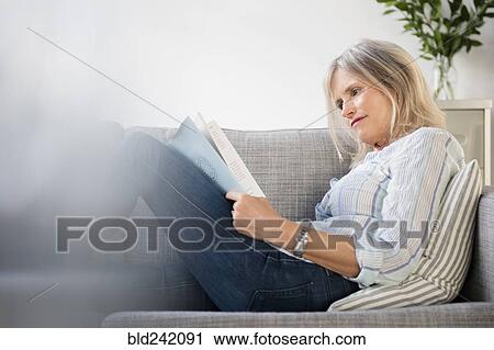 Stock Image - Serious Caucasian woman sitting on sofa reading paperwork. Fotosearch