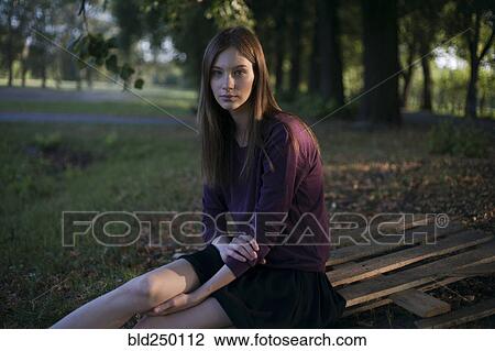 Stock Image - Serious Caucasian woman sitting on wooden pallet in park. Fotosearch