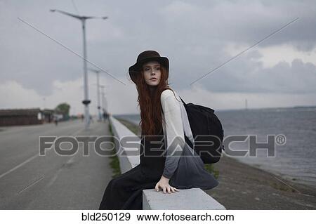 Serious Caucasian woman sitting on wall near ocean View Large Photo Image Stock Photo - Serious Caucasian woman sitting on wall near ocean. Fotosearch