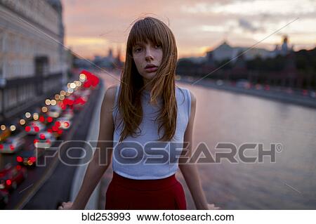 Stock Image - Serious Caucasian woman standing at urban waterfront. Fotosearch